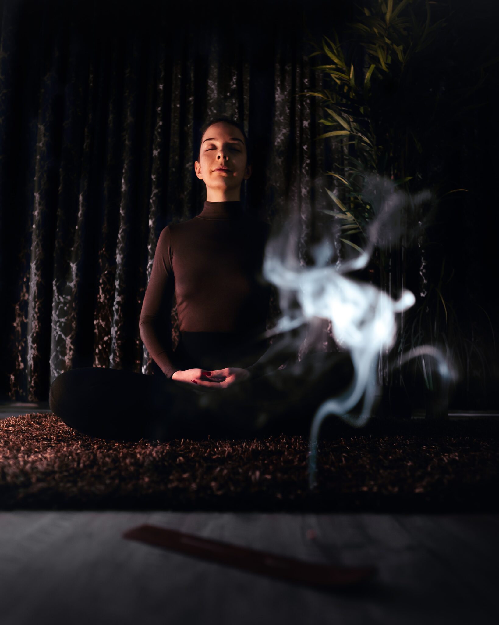 woman with short hair meditating in dark room with incense burning