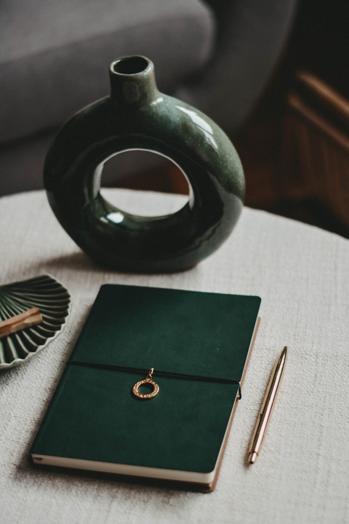 green journal and vase on a white desk with gold pen