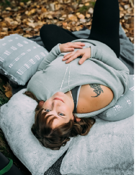brunette woman with gray sweater laying upside down bolstered by pillows in fall leaves
